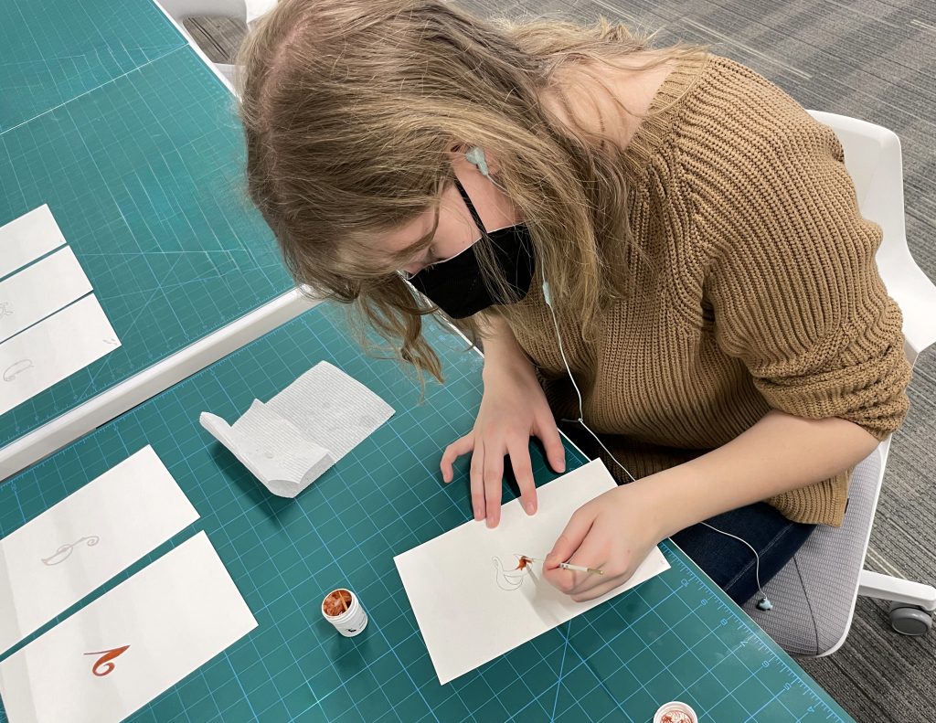 A student painting on paper different font styles.
